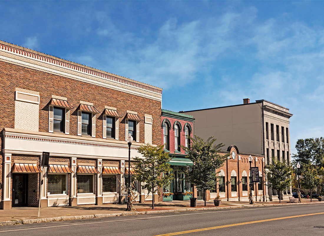 Bryan, OH - Row of Commercial Buildings Against a Blue Sky in Downtown Bryan Ohio with an Empty Road and Green Trees Along the Sidewalk