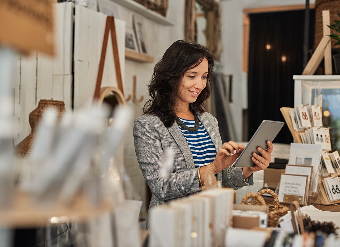 Business Insurance - Portrait of a Cheerful Middle Aged Business Woman Using a Laptop While Standing in her Small Boutique Shop