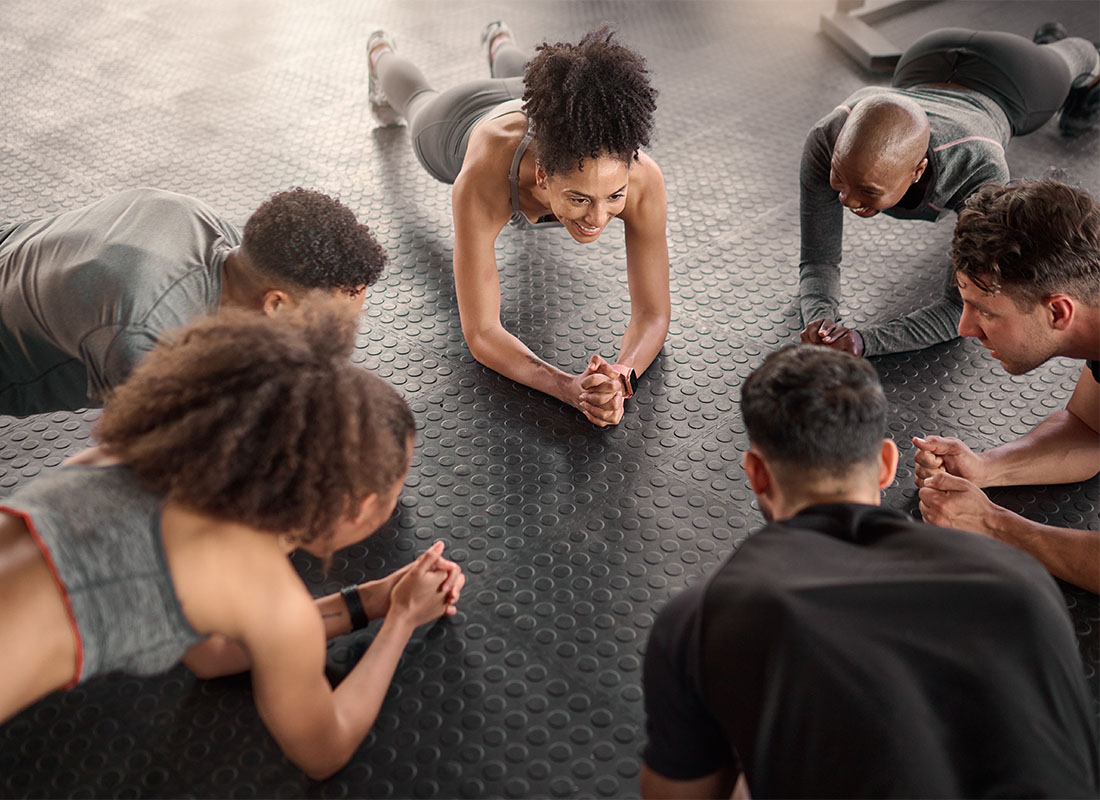 Employee Benefits - Small Group of Smiling Diverse People Doing Planks During a Workout Session in the Gym