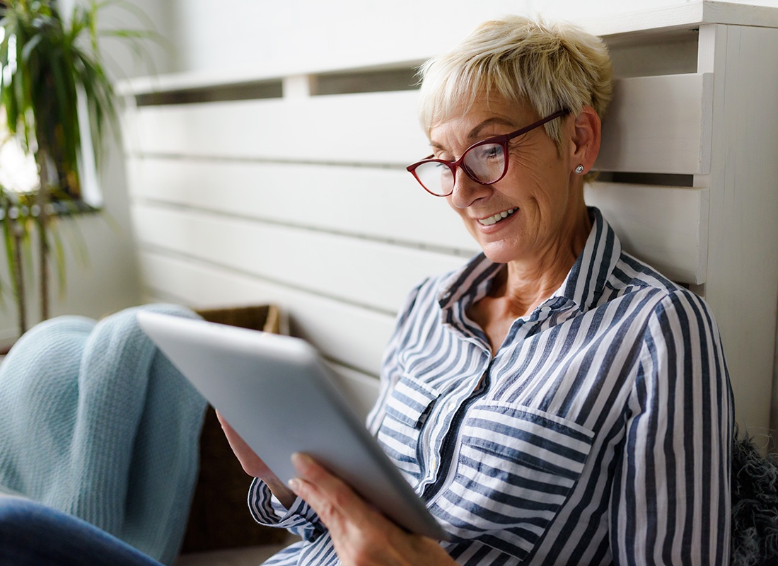 FAQs - Closeup Portrait of a Senior Woman with Glasses Sitting at Home While Reading on a Tablet