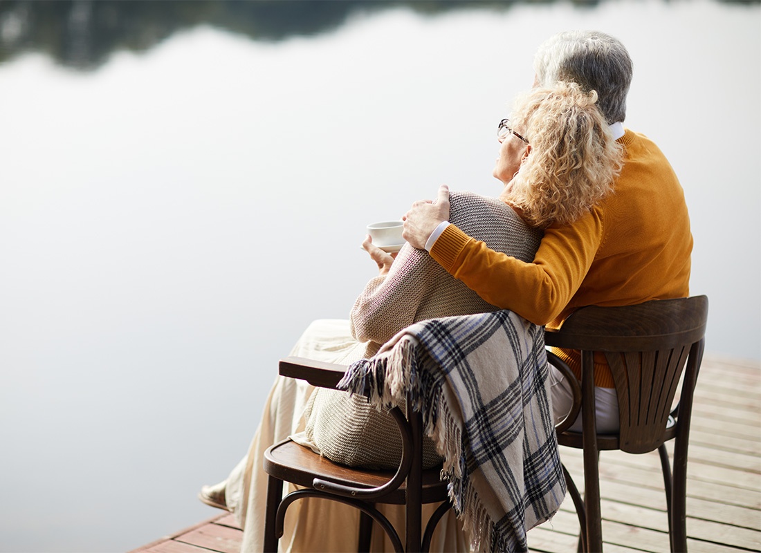 Medicare - Rear View of a Loving Elderly Couple Sitting on Chairs on a Wooden Dock While Enjoying the Views of the Lake on a Sunny Fall Day